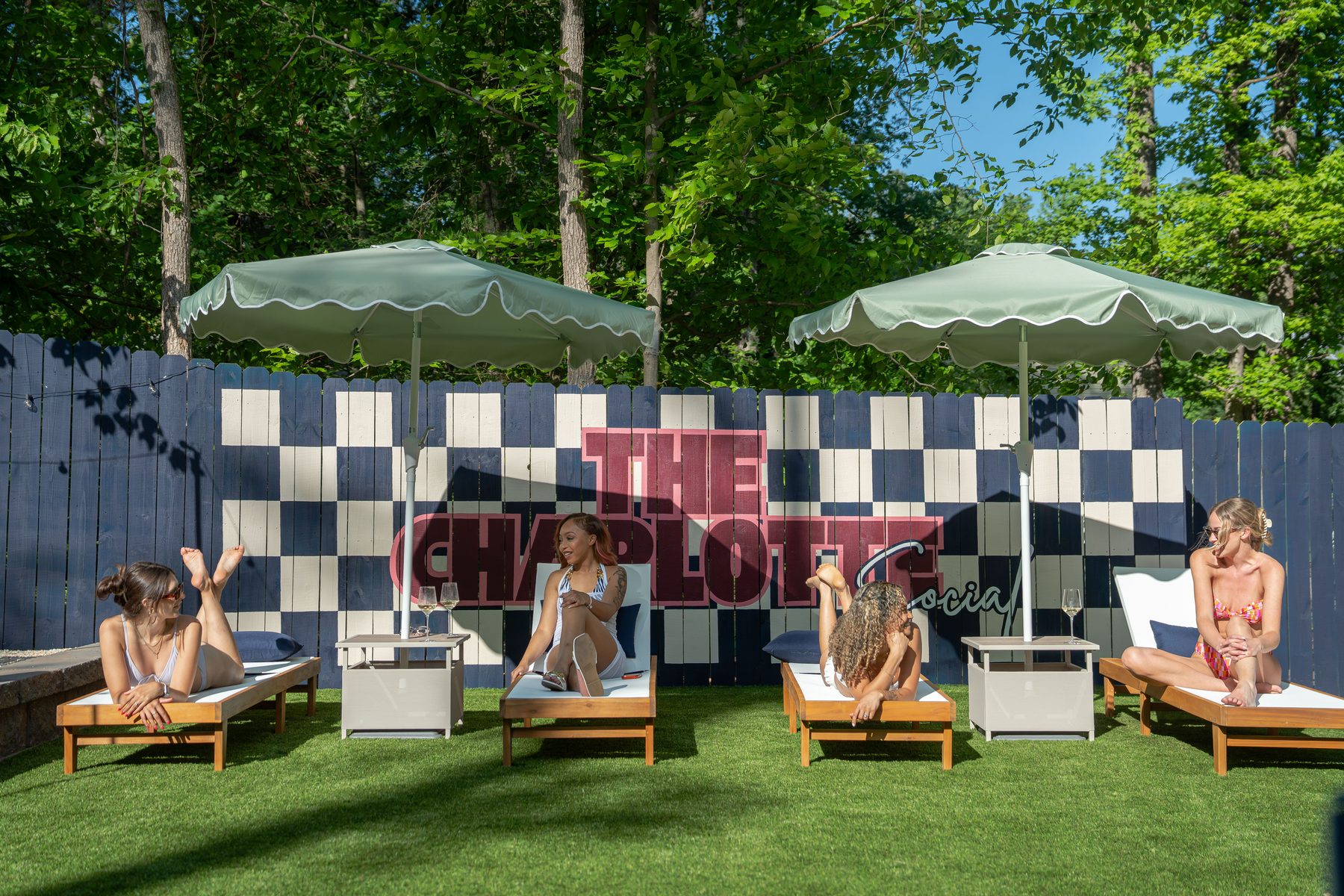 A group relaxing on loungers in front of the branded checkerboard wall at The Charlotte Social